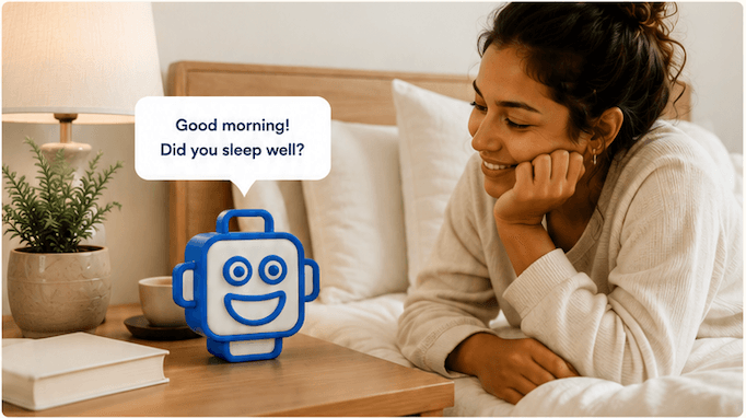 A woman smiling while talking with the soft blue NED device on a bedside table.